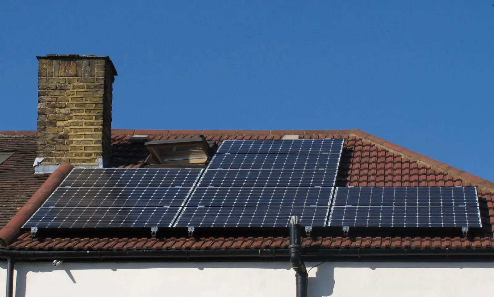 Solar PV panels fitted in place on a tiled pitched roof beneath a chimney