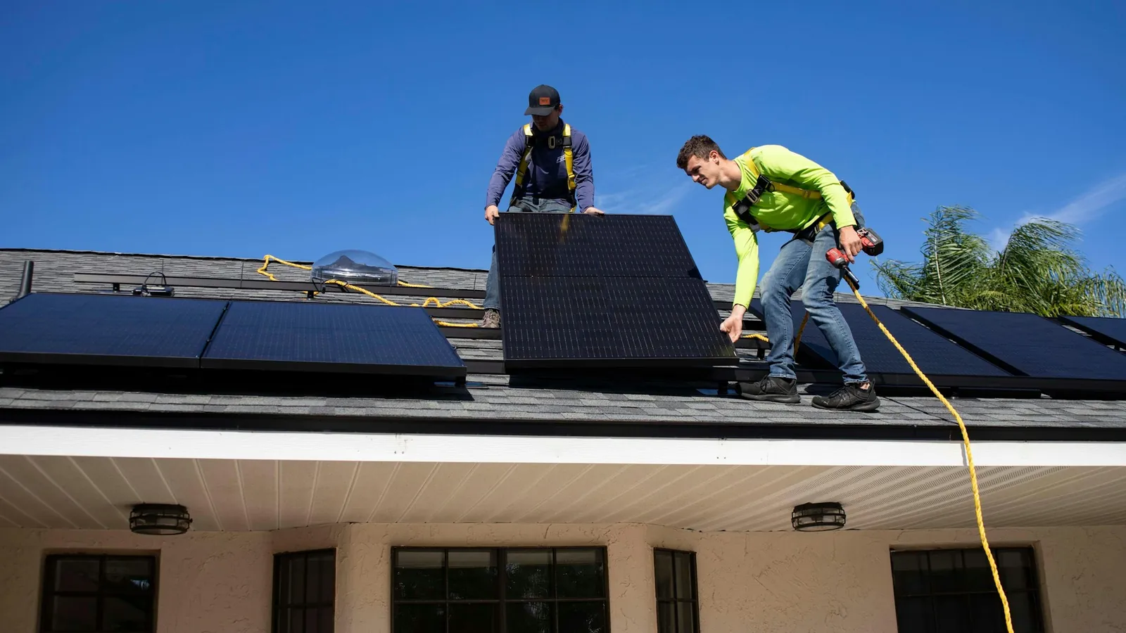Two installers carrying a solar panel across a pitched roof