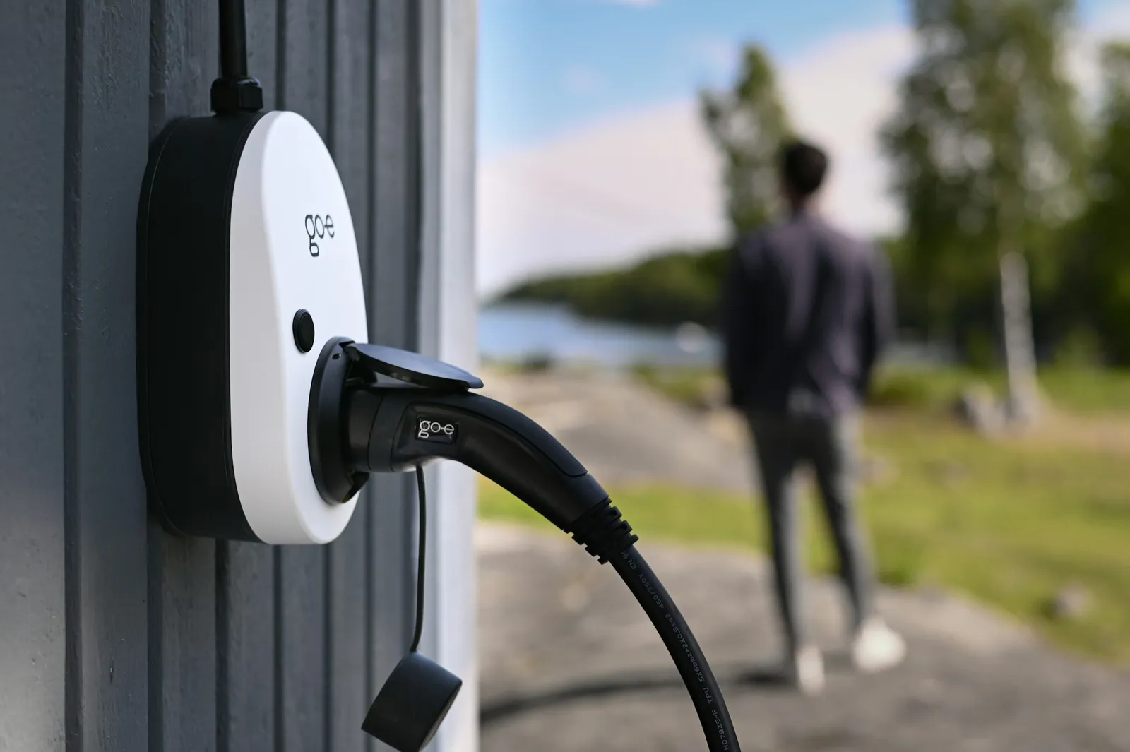 A white wall-mounted EV charger with its charging cable beside a house