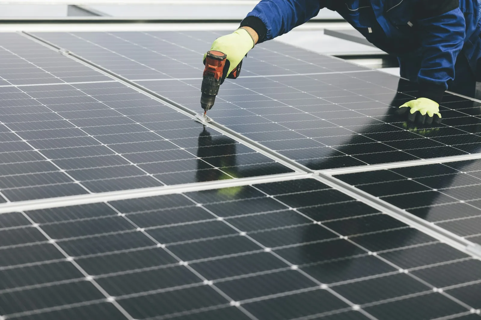 A technician using a drill to fix a solar panel in place on a rooftop array
